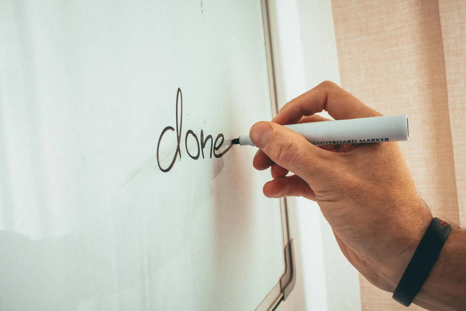 Käsi kirjutab valgele tahvlile sõna „done“